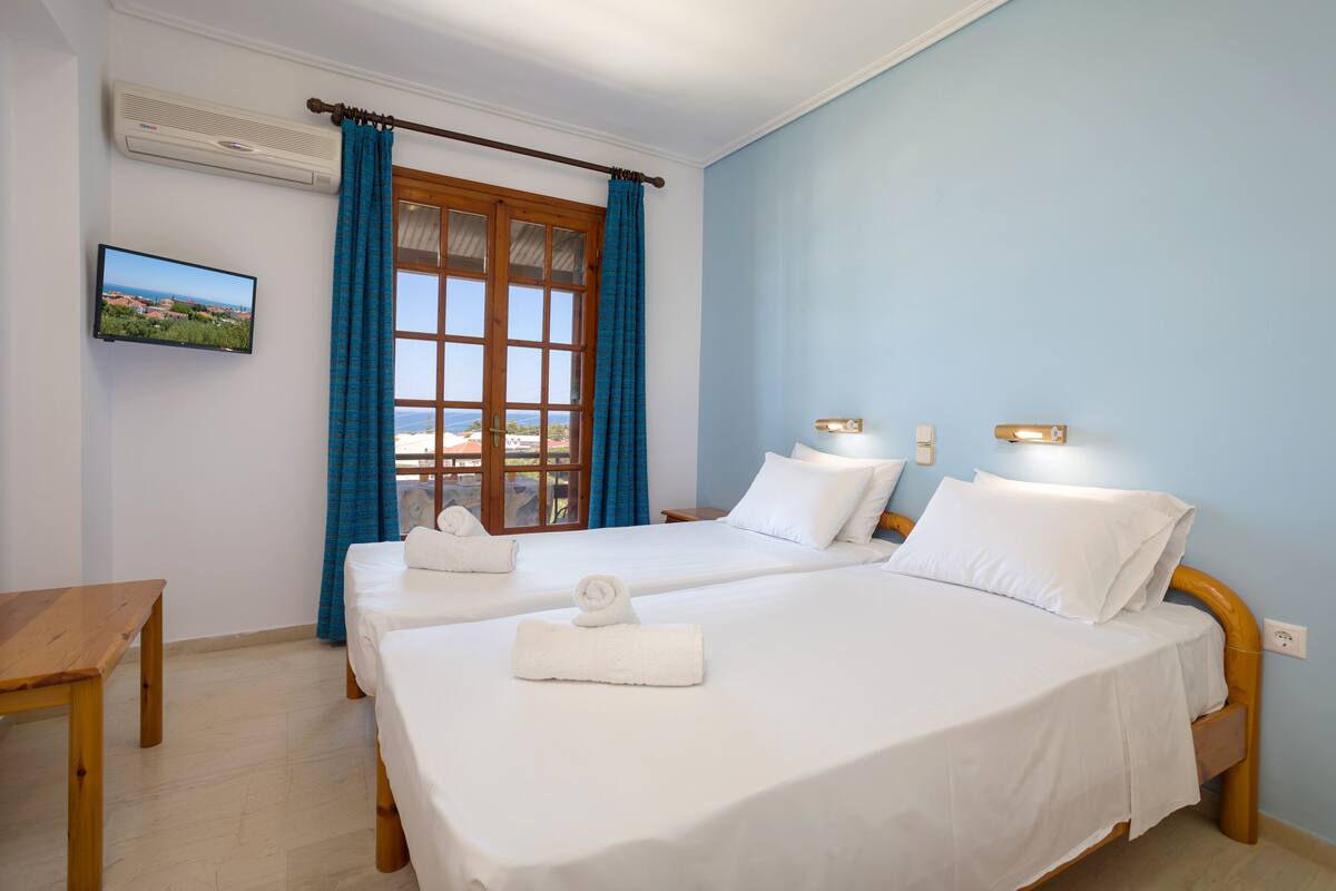 A hotel room with two beds, a TV, a wooden table, and a window with curtains.