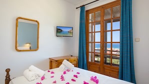 A hotel room with a bed, a wooden dresser, a mirror, a television, and a window with curtains. - Vallia's Apartments (Zakynthos)