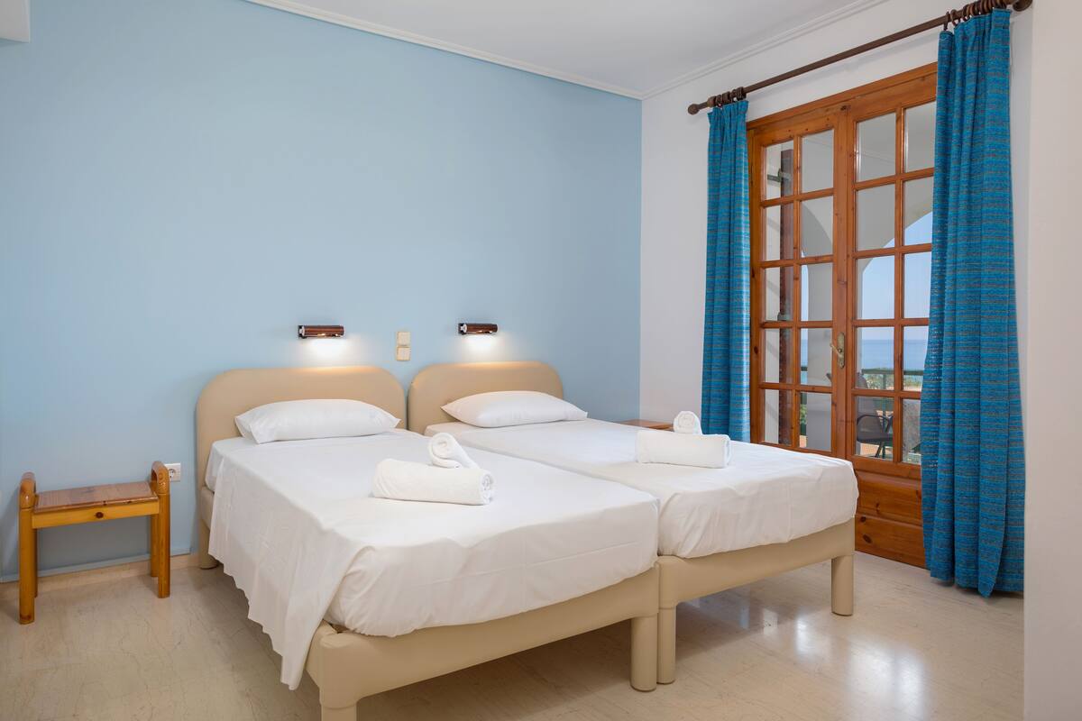A room with two beds, a wooden bench, and a window with curtains.