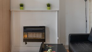 A living room with a black sofa, a small table with a green plant, and a vintage radio. - Tower Bridge Accommodation - 5 (London)