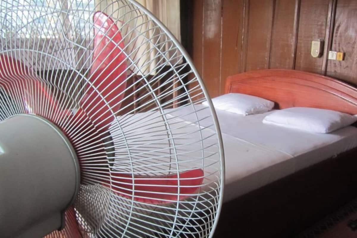 Ein Zimmer mit einem Bett, einem weißen Ventilator und Holzwänden.