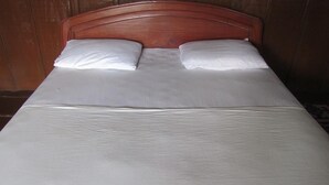 Uma cama com cabeceira de madeira, duas almofadas e um edredom branco.