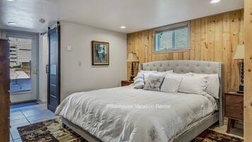 A bedroom with a large bed, wooden panel walls, a window, and a door leading outside.
