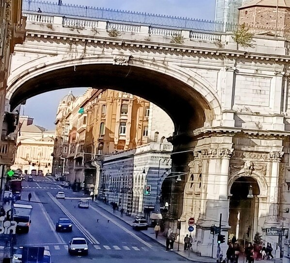 Una calle bajo un gran puente de piedra con arquitectura clásica, incluyendo columnas y detalles decorativos.