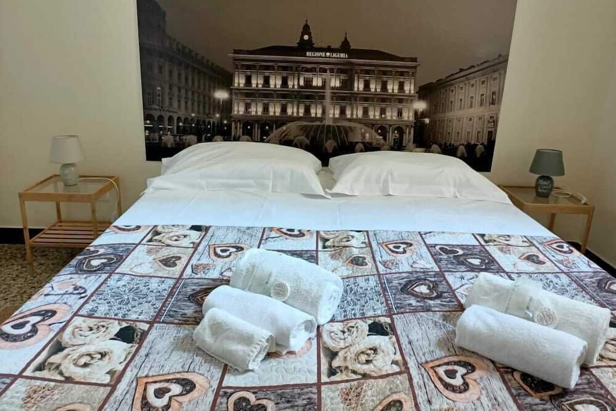 A hotel room with a large bed, two bedside tables, and a wall tapestry depicting a building.