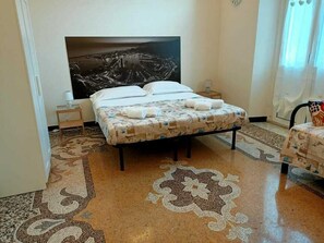 Habitación de hotel con una cama grande, una mesita de noche, una lámpara y vistas a la ciudad por la ventana.
