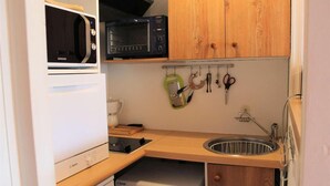 A compact kitchen with a microwave, toaster, sink, and a drying rack.