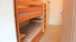 A bunk bed in a narrow room with a door and a light switch on the wall.