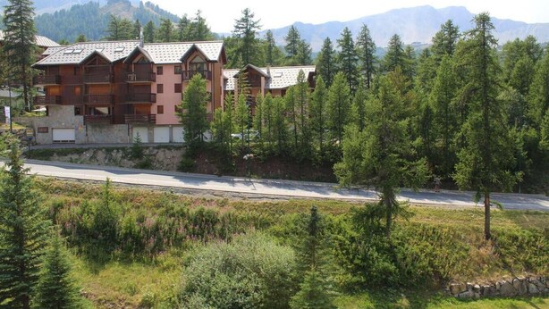 A lodge with multiple wooden buildings, surrounded by dense forest and mountains in the background.