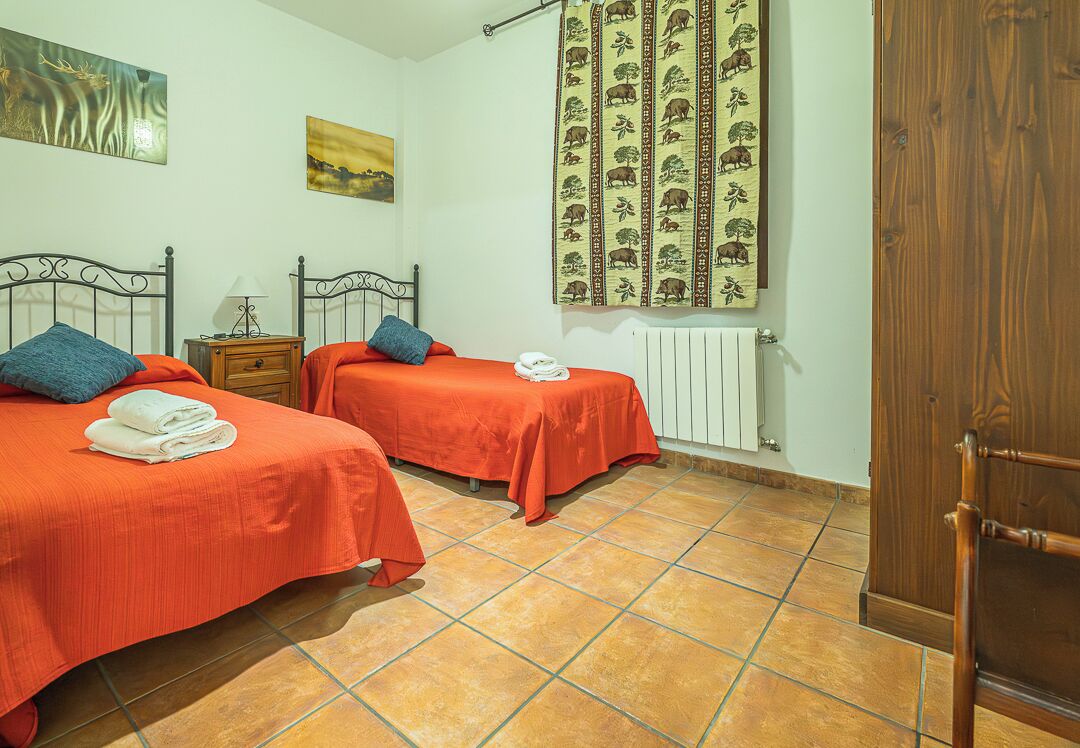 A bedroom with two beds, a wooden nightstand, a radiator, and a door.
