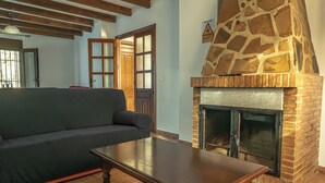 A living room with a stone fireplace, a sofa, and a wooden coffee table. - Casa Rural Mirador de los Tomillos (Cardena)
