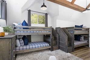 A bunk bed room with a window, wooden staircase, and a desk with drawers.