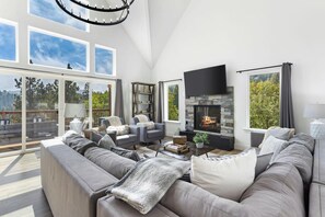 A modern living room with a fireplace, large windows, and a cozy seating area. - New Home 2 Mstrs, AC, EV Chgr, Pool Table, Lake Rights (Lake Arrowhead)