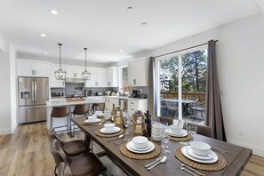 A modern kitchen with white cabinets, stainless steel appliances, and a dining area set for a meal with a view of the outdoors.