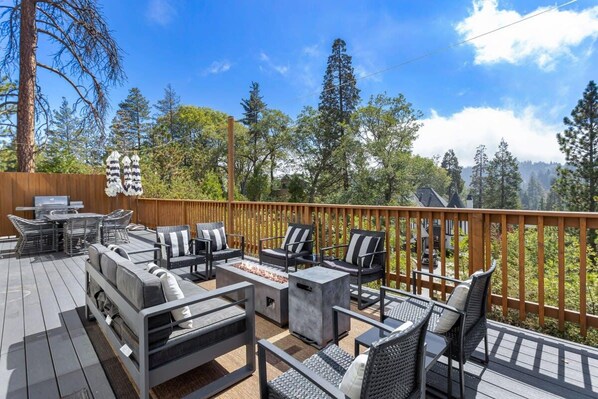 A deck with outdoor furniture, a fire pit, and a view of a forested area.