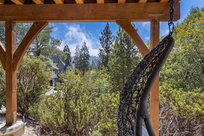 A wooden pergola structure with a hanging net, surrounded by dense green foliage and a house in the background.