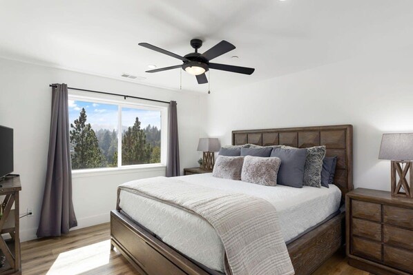A bedroom with a bed, a ceiling fan, a nightstand, a lamp, and a window with curtains.