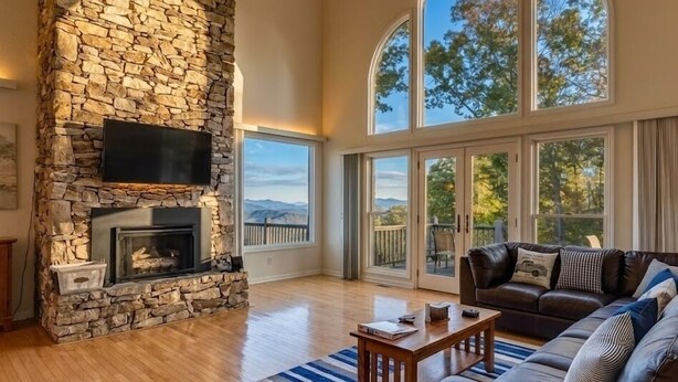 A living room with a stone fireplace, a leather sofa, a coffee table, and large windows offering a view of the outdoors. - 10 Min TO DT, 16 min to Biltmore, Lg Home,  Apartment Incl., Peaceful & Quiet (Asheville)