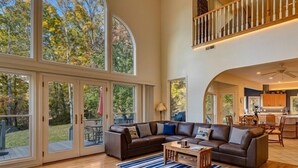 A spacious living area with a large sectional sofa, a coffee table, and a view of the outdoors through large glass doors. - 10 Min TO DT, 16 min to Biltmore, Lg Home,  Apartment Incl., Peaceful & Quiet (Asheville)