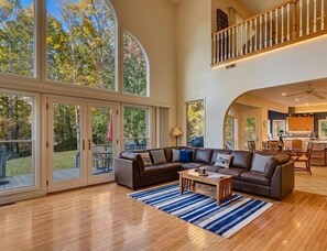 A spacious living area with a large sectional sofa, a coffee table, and a view of the outdoors through large glass doors.