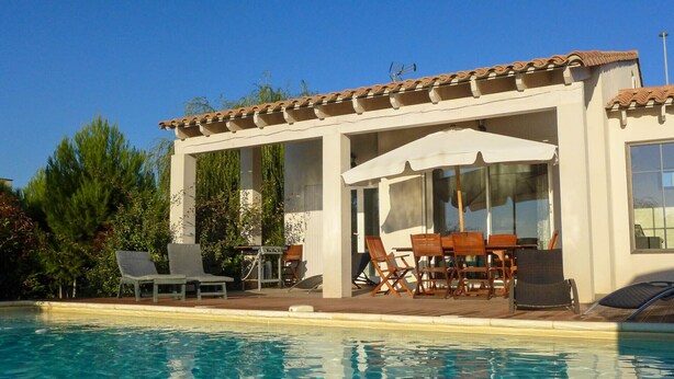 A poolside area with a covered seating area, a table, and chairs. - Nice quiet house classified 3* in Narbonne with private overflowing pool (Narbonne)