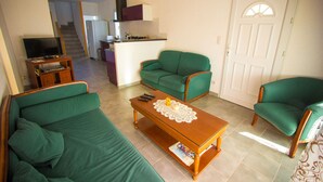 A living room with green sofas, a wooden coffee table, and a television on a stand. - Nice quiet house classified 3* in Narbonne with private overflowing pool (Narbonne)