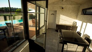 A room with a glass door leading to a pool area, a dining table with chairs, and a view of the pool. - Nice quiet house classified 3* in Narbonne with private overflowing pool (Narbonne)