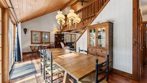 Un comedor amplio con una mesa y sillas de madera, un candelabro y una escalera que lleva a un nivel superior.