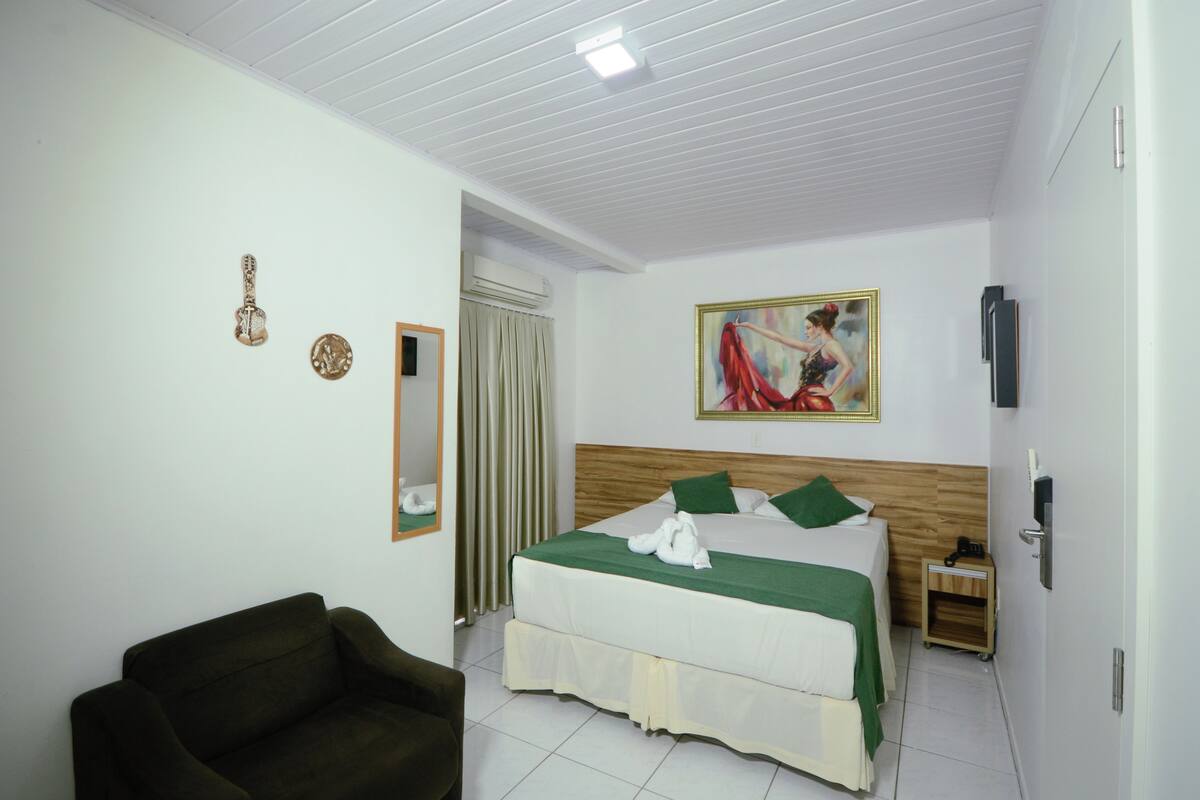 Une chambre d’hôtel avec un lit, une chaise, un tableau, un miroir et une petite table d’appoint en bois.