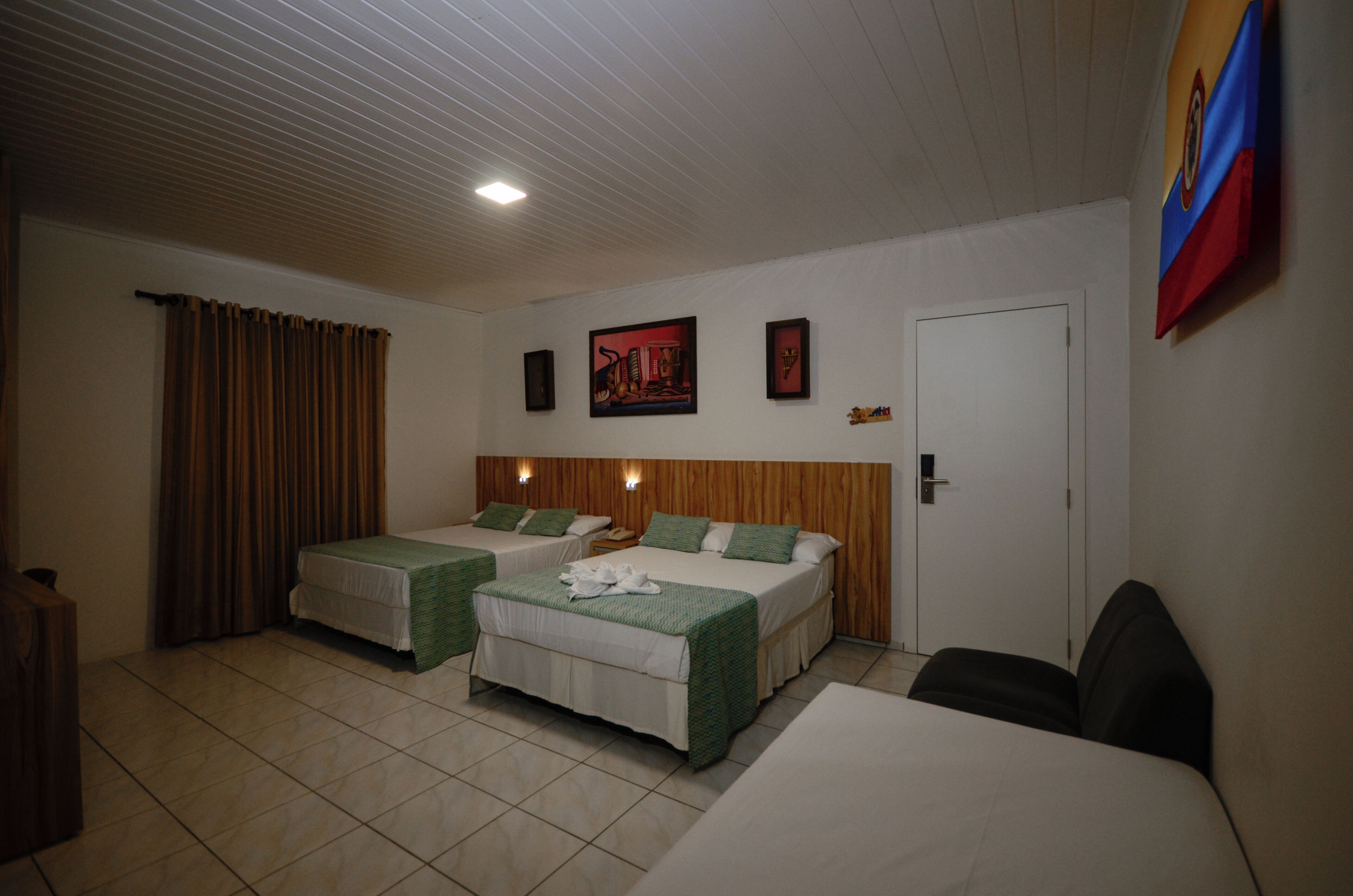 Habitación de hotel con dos camas, cabecero de madera, una puerta y una pared decorada con cuadros.