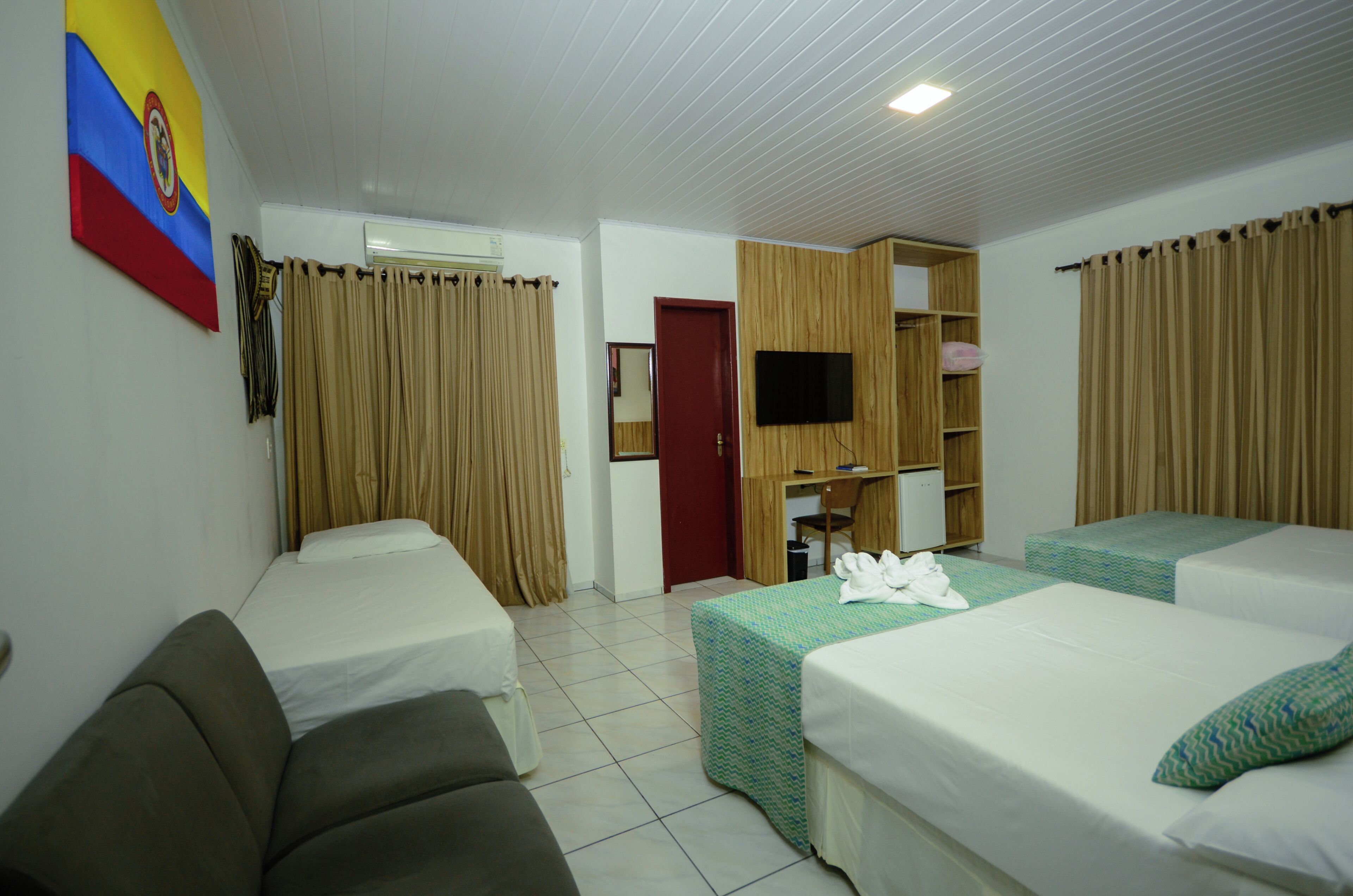 A hotel room with two beds, a sofa, a TV, a desk, and a wardrobe.