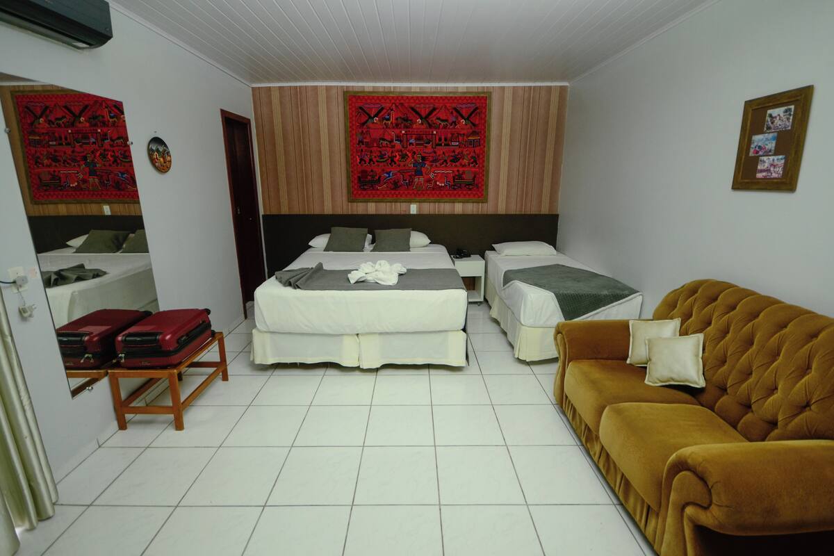 Une chambre d’hôtel avec deux lits, un canapé, une petite table sur laquelle sont posées des valises, et des œuvres d’art décoratives accrochées au mur.