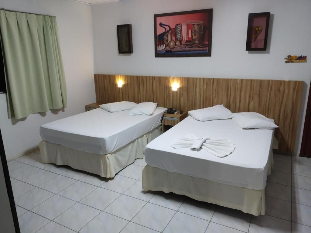 A hotel room with two beds, a wooden headboard, a painting on the wall, and a curtain.