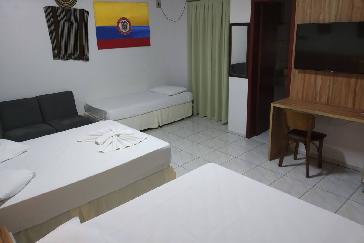 Une chambre d’hôtel avec un lit, un canapé, un bureau, une télévision et un drapeau accroché au mur.