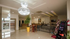 A hotel lobby with a reception desk, a chandelier, a potted plant, a sofa, and a digital information kiosk. - Hotel Iguacu (Dionisio Cerqueira)