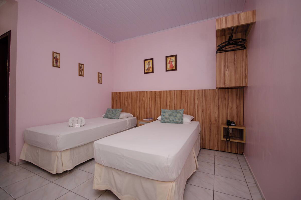 Une chambre avec deux lits simples, une tête de lit en bois, une petite armoire en bois et un porte-manteau fixé au mur.