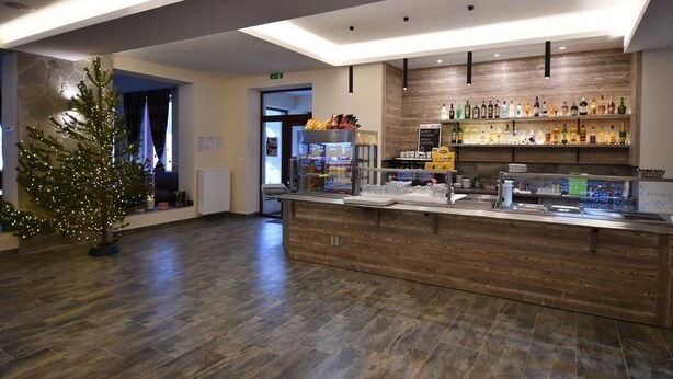 A modern hotel lobby with a wooden reception desk, a Christmas tree, and a bar area with various bottles. - Hotel Studničky (Vernár)
