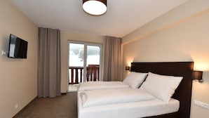 A hotel room with a bed, a TV, a balcony with curtains, and a ceiling light. - Hotel Studničky (Vernár)