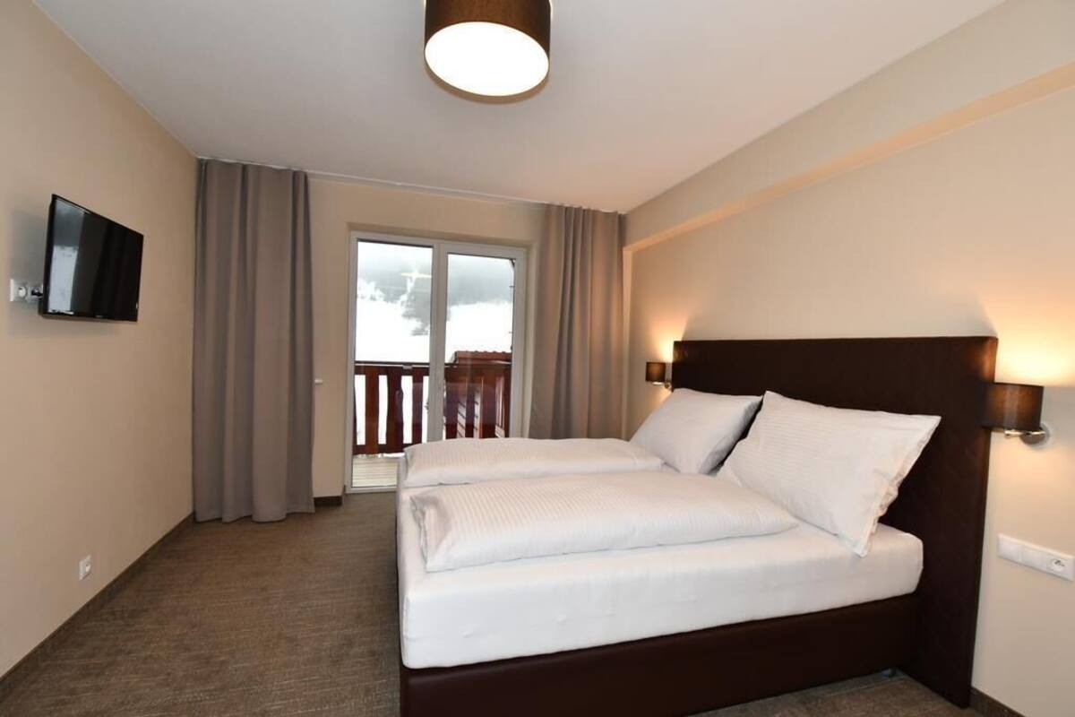 Una habitación de hotel con cama, televisión, balcón con cortinas e iluminación en el techo.