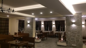 A dining area with wooden tables and chairs, stone pillars, and recessed lighting. - Hotel Studničky (Vernár)