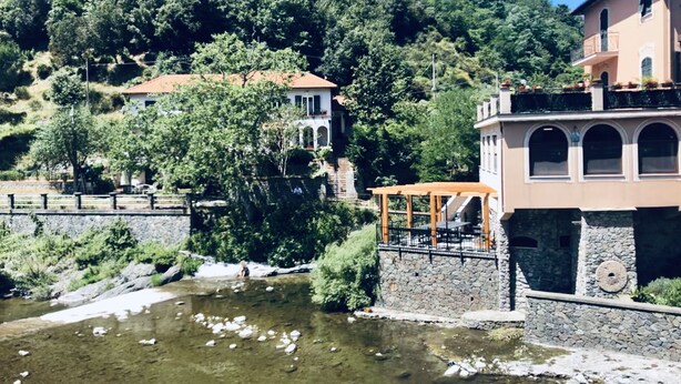 A riverside view with a stone bridge, a gazebo, and buildings with arched windows. - La casa sul fiume (Ellera)