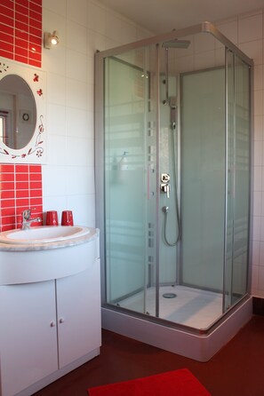 A modern bathroom with a glass-enclosed shower, a white sink with a red accent wall, and a mirror with a decorative frame. - B&B Aux Berges de la Thur (Staffelfelden)