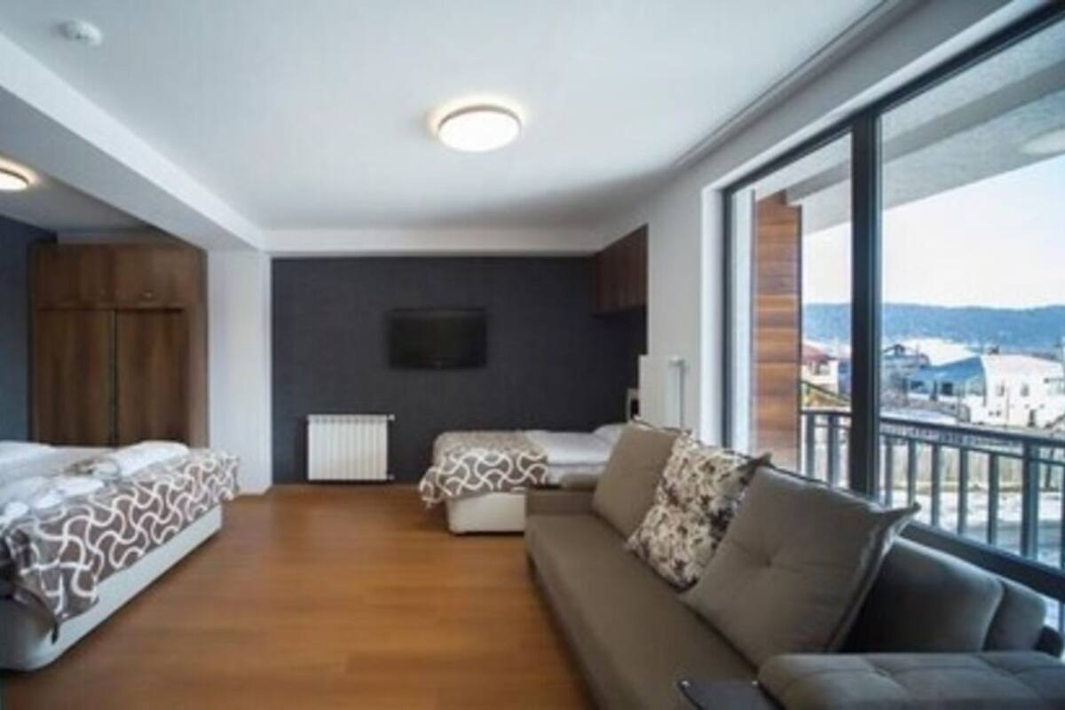 Un apartament modern amb un balcó gran, un sofà, dos llits i una televisió.