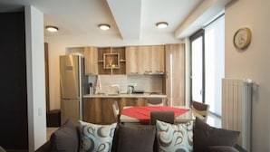 A compact kitchen with wooden cabinets, a stainless steel refrigerator, and a dining area with a red tablecloth. - Apartments Nadim (Skopje)
