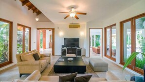 Uma sala de estar ampla com uma televisão grande, assentos confortáveis e grandes janelas com vista para o exterior.