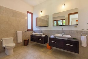 A modern bathroom with two sinks, a toilet, and a large mirror.