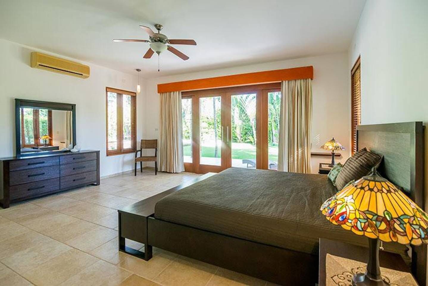 A bedroom with a bed, a dresser, a chair, a ceiling fan, and a window with curtains.