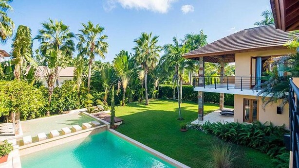 Piscina com espreguiçadeiras, cercada por vegetação exuberante e palmeiras.