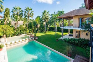 A swimming pool with a deck, surrounded by lush greenery and palm trees.