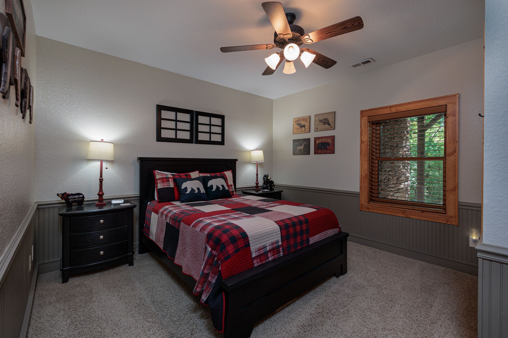 A bedroom with a bed, two bedside tables, a ceiling fan, and a window with a view of trees.